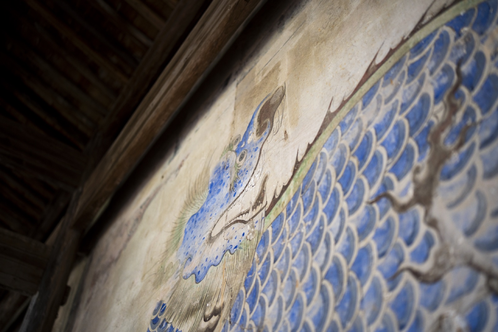 A faded blue dragon mural painted inside the village pagoda.