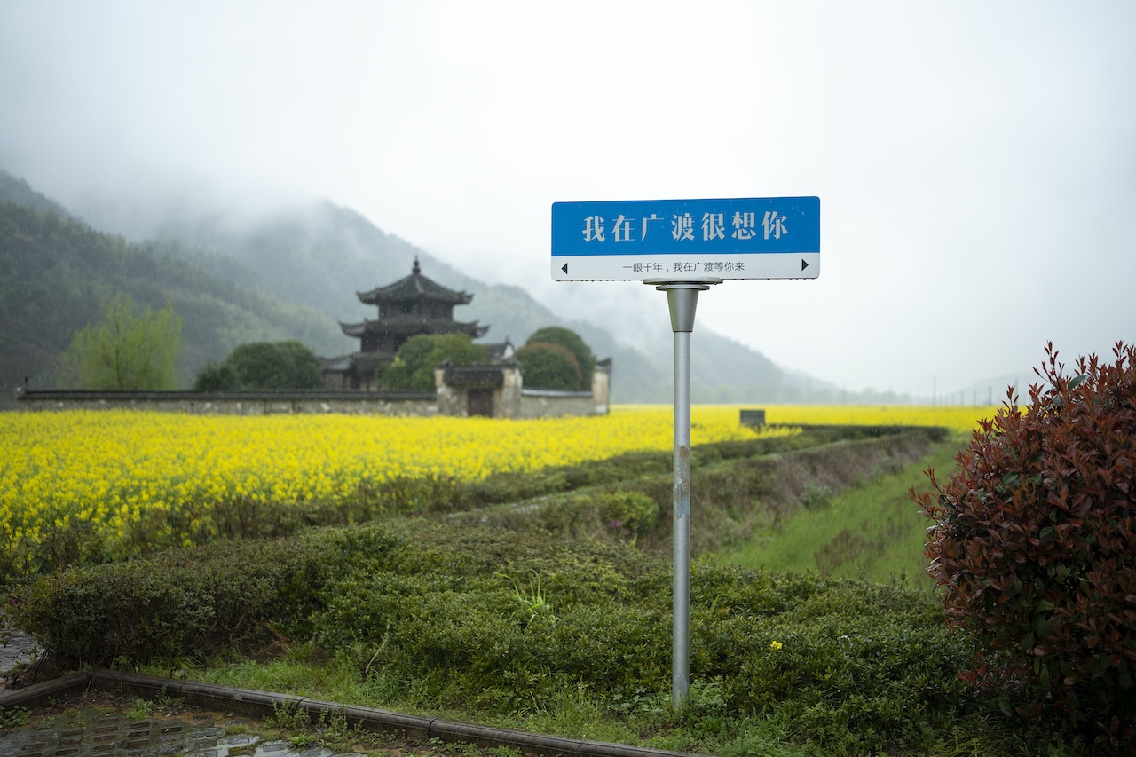 A roadside sign reading “I miss you in Guangdu” beside the village’s old pagoda and fields of rapeseed flower.